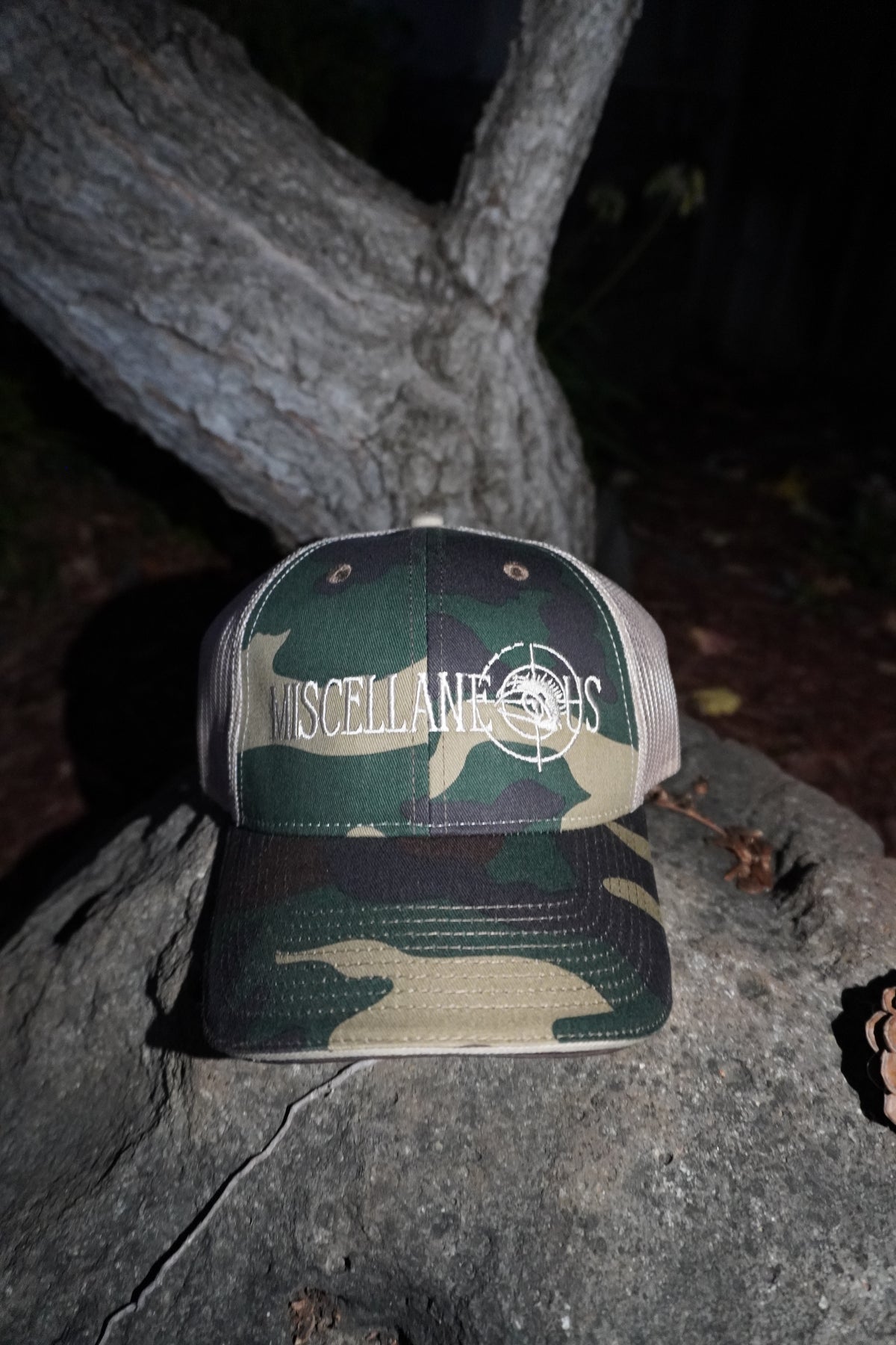 Green camo trucker hat with tan mesh back and white embroidered Miscellaneous logo