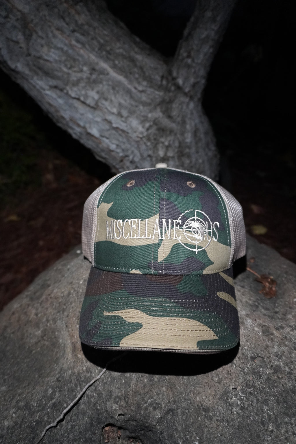 Green camo trucker hat with tan mesh back and white embroidered Miscellaneous logo